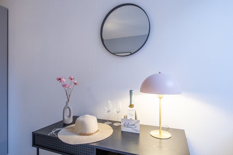 Desk with hat, lamp, flower vase, wine glasses, bottle, welcome card, mirror on wall