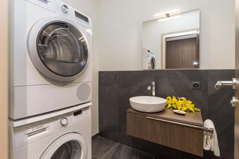 modern bathroom with stacked washing machines, round sink, small shelf, mirror, towel rack