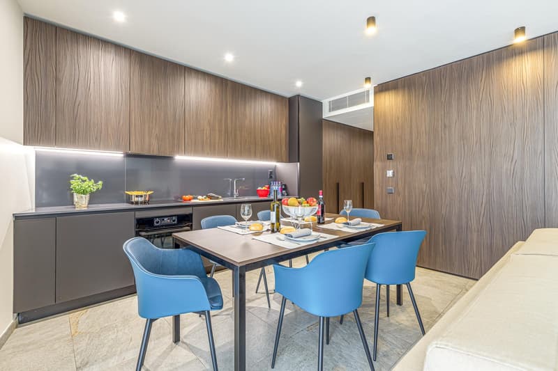 modern kitchen with wooden cabinets, tile flooring, dining table with blue chairs, open to living area