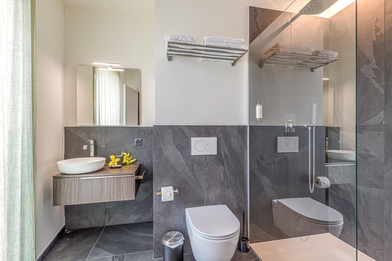 modern style bathroom, white sink, white toilet, open shower, towel racks, gray tiles