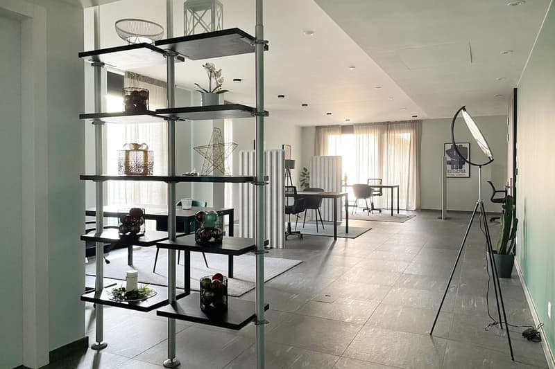Modern, open, large room with high ceilings, large windows, tables, chairs, and shelves with decorative objects.