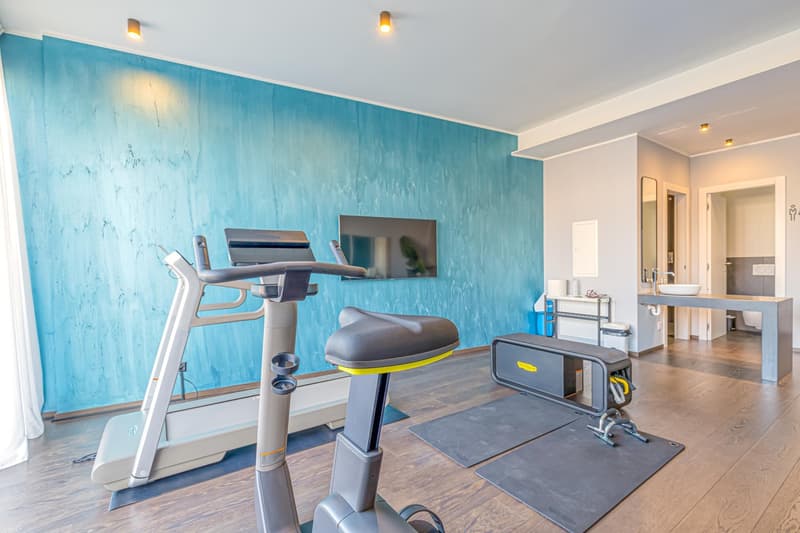 small room with wooden floor, blue wall, gym machines, bench, mirror, white door, sink, tv