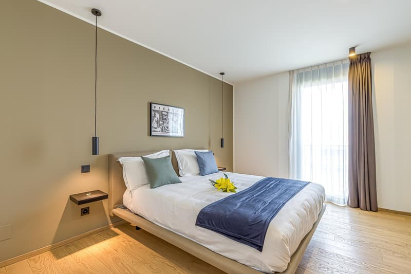 double bed, beige walls, wooden floor, window, yellow flower on bed, picture on wall