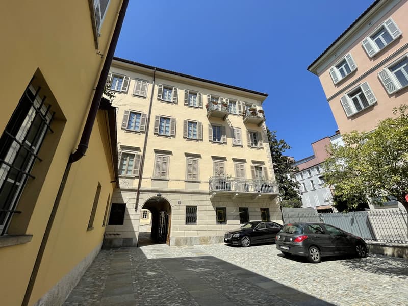 4 story building, beige exterior, multiple balconies, arched entrance, two cars parked in front
