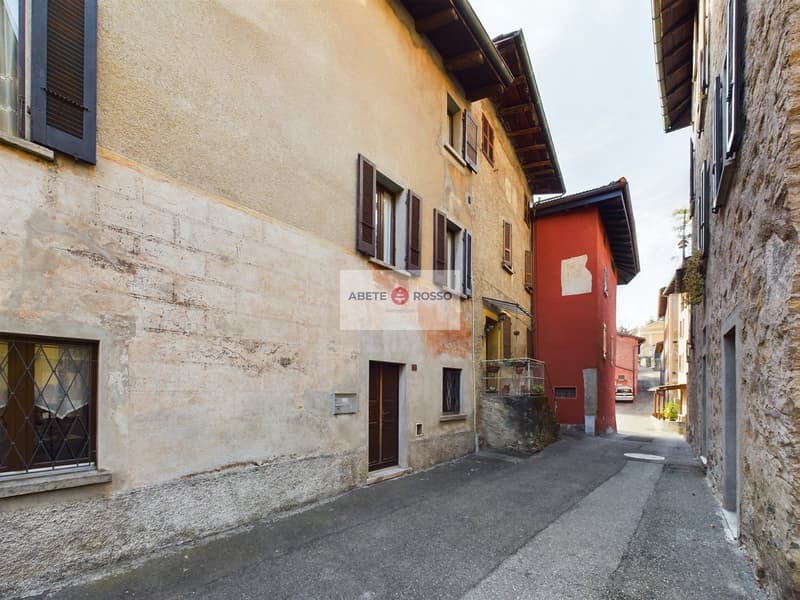 Narrow cobblestone street with old stone buildings, some with red walls, wooden shutters, and a sign for 'Abete Rosso' on the building.