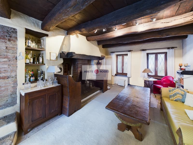 Rustic living room with exposed wooden beams, brick fireplace, wooden furniture, and shelves displaying bottles and glassware