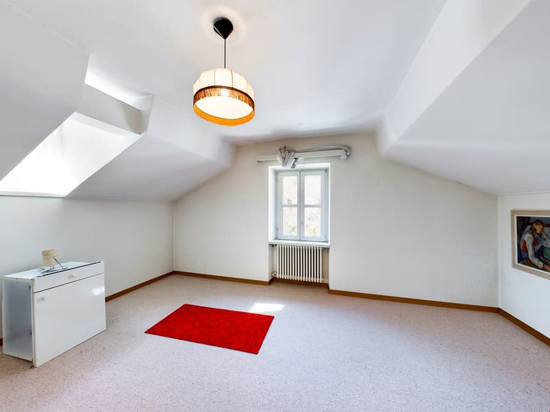Attic room with white walls, hardwood floor, large window, pendant light fixture, and a red rug on the floor.