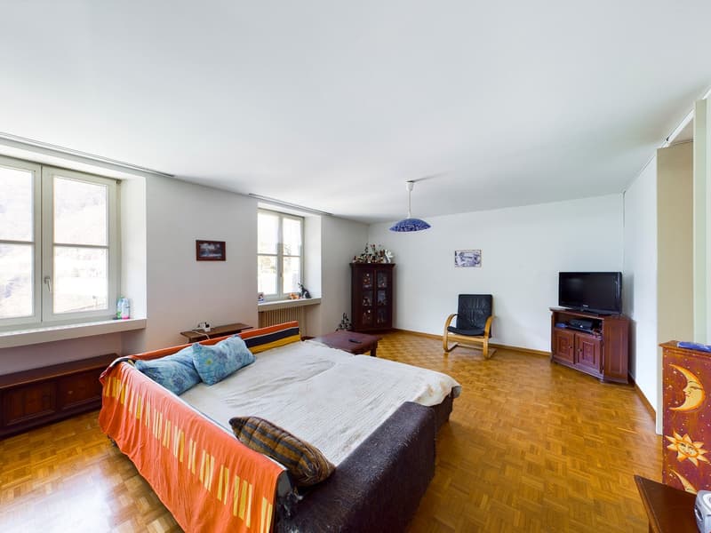 large bed, pillows, brown armchair, wooden side tables, flat screen TV, wooden flooring, windows, picture frames, cabinet