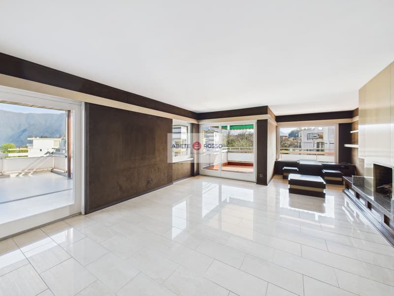 Spacious open-plan living room with large windows, sliding glass doors leading to a balcony, hardwood floors, and a modern entertainment unit