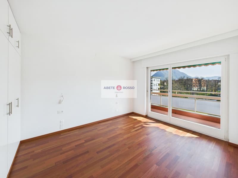 Spacious living room with hardwood flooring, large windows providing a scenic view, and a balcony or terrace accessible from the room.