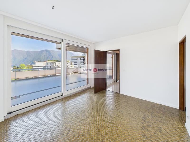 Spacious living room with large windows offering a scenic view of the mountains, hardwood-patterned tile flooring, and a sliding glass door leading to a balcony or terrace.