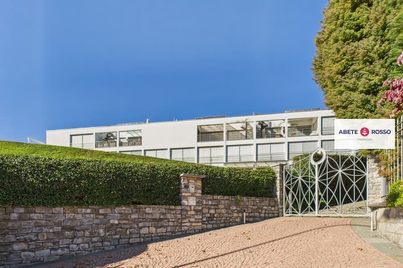 Modern apartment building, white facade, balconies, green hedges, entrance gate
