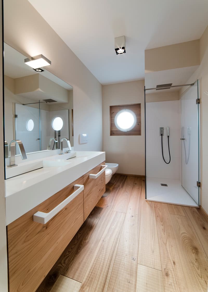 double sink, wooden cabinets, round window, walk-in shower, built-in shower head, toilet