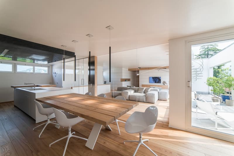 dining area with wooden table, white chairs, open to living room with sofa and couch, sliding glass door to balcony, large glass wall, modern kitchen island with sink