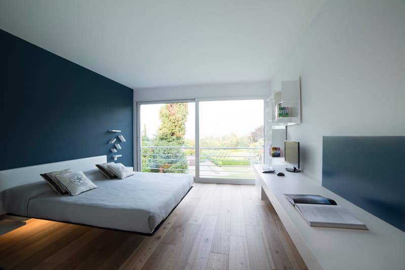 Large bed, bedside tables, sliding doors to balcony, modern decor, white and blue color palette