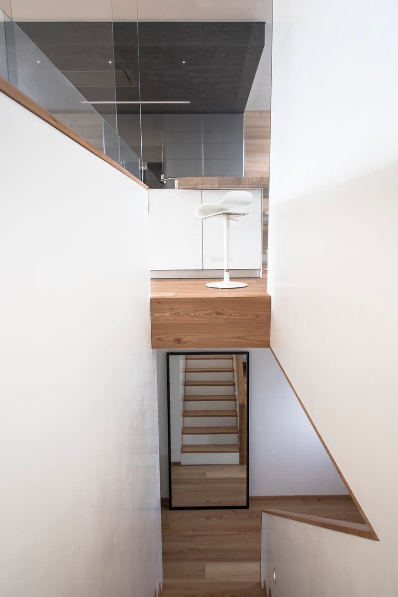 staircase with wooden steps and white walls, mirror on one side, white cabinet and white stool