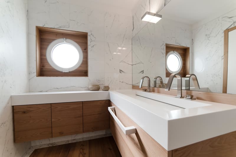 Modern bathroom, marble wall tiles, two windows, white sinks, wooden cabinets, modern faucets