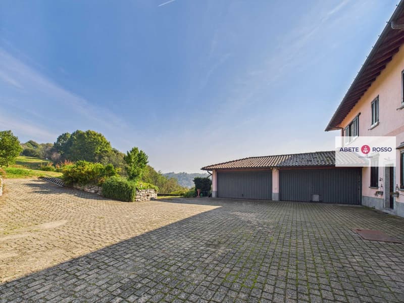Detached house with garage, brick driveway, garden, trees, hills in the distance