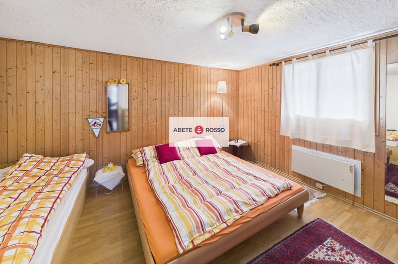 Bedroom with two beds, wooden walls, white curtains, radiator, lamp, mirror, rug, nightstands, and decorative items.