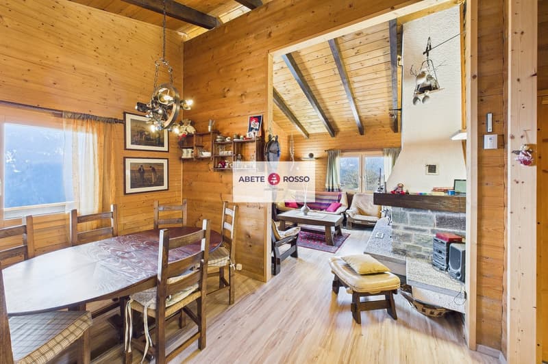 Dining room with wooden table and chairs, wooden walls, fireplace, shelves with items, window with curtains