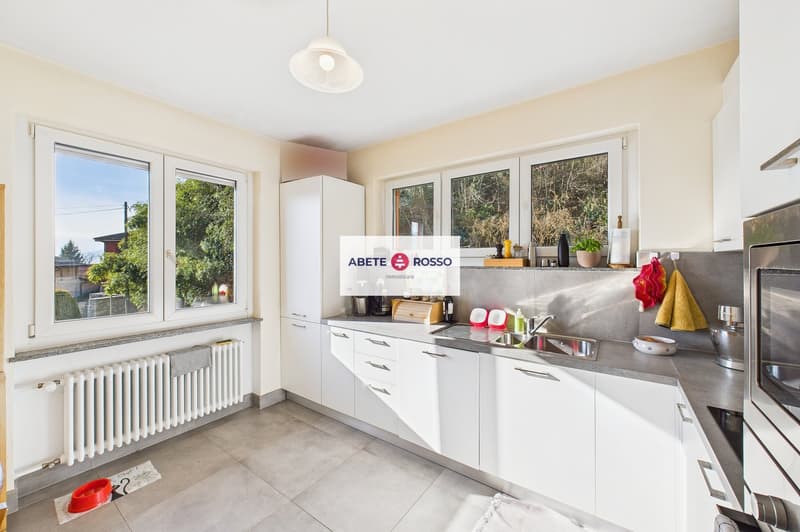 modern kitchen with white cabinets, gray countertops, stainless steel sink, large windows, radiator, hanging towels, hanging kitchen utensils