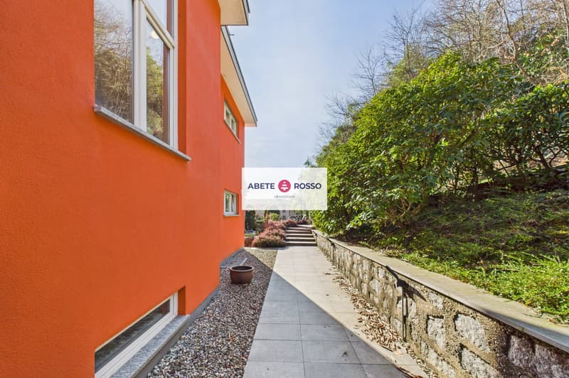 Orange exterior wall, white windows, gravel pathway, stone wall, greenery