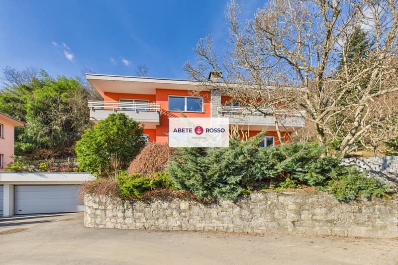 Two-story house, orange exterior, white garage, stone wall, balcony, trees, bushes