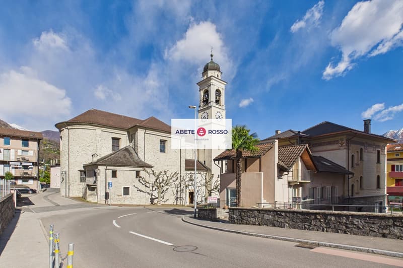 Church with a tower, surrounded by buildings, street with a curve, stone wall, clear sky