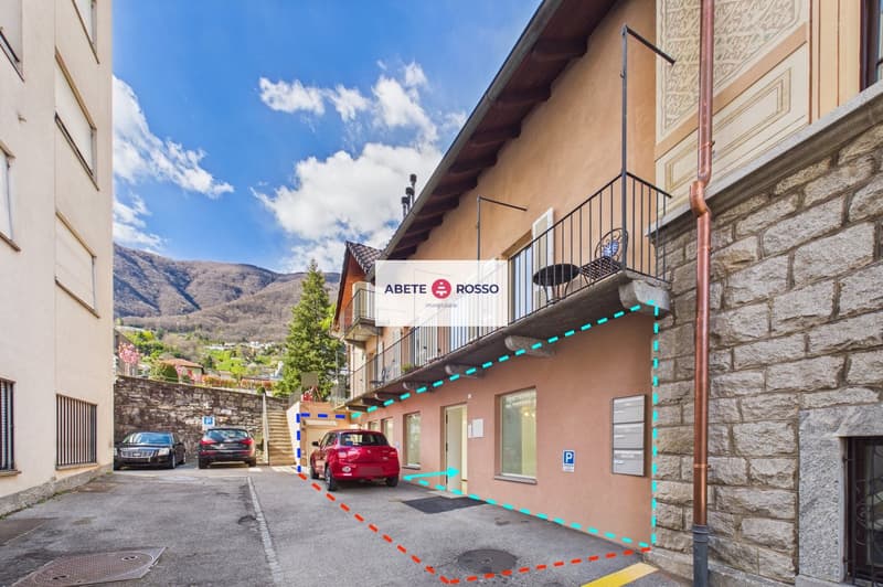Building with balcony, parking area, and a red car parked in front