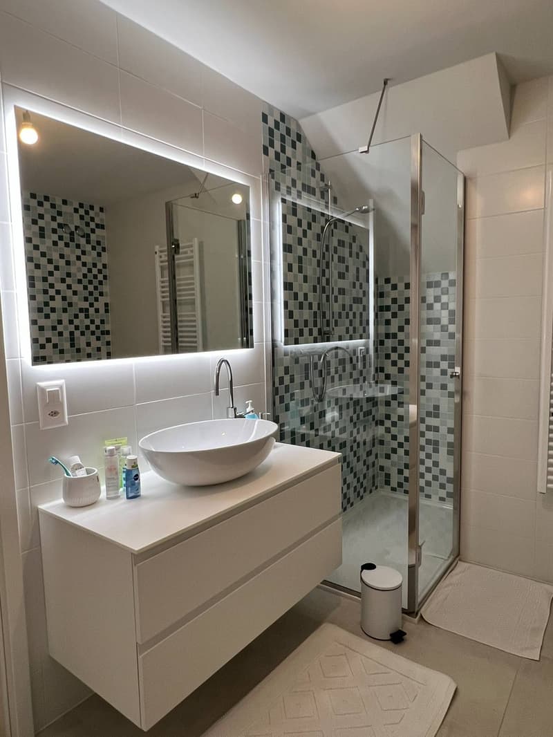 Modern bathroom with white vanity, vessel sink, tiled walls with black and white mosaic pattern, shower enclosure, and towel rack
