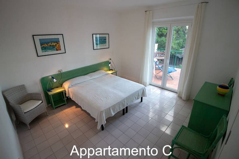 large bed, two nightstands with lamps, armchair, glass door to terrace, tile floor, green walls