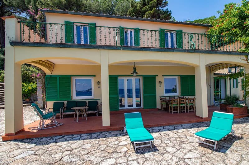 Two-story house, green shutters, ocean view, stone patio, green lounge chairs, outdoor dining table, stone walkways