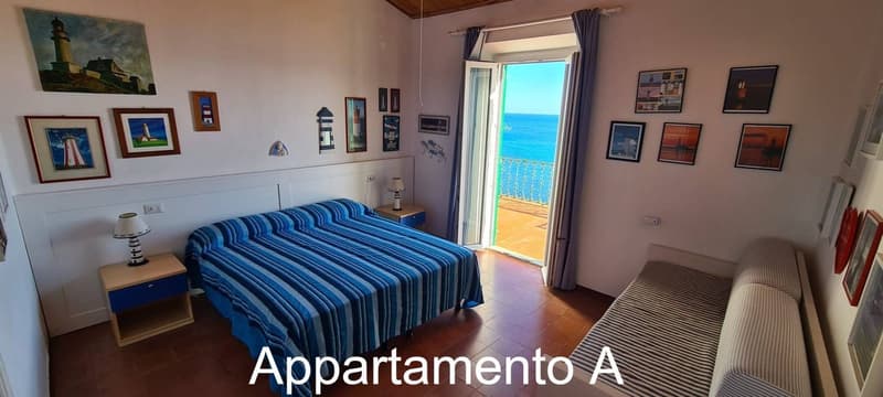 Double bed, nightstand, lamp, framed pictures, couch, open sliding doors, balcony with railing, ocean view