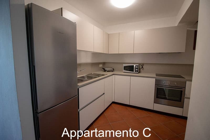 Modern kitchen with appliances like a refrigerator, sink, microwave, oven, and dishwasher. Tiled floor and white cabinetry.