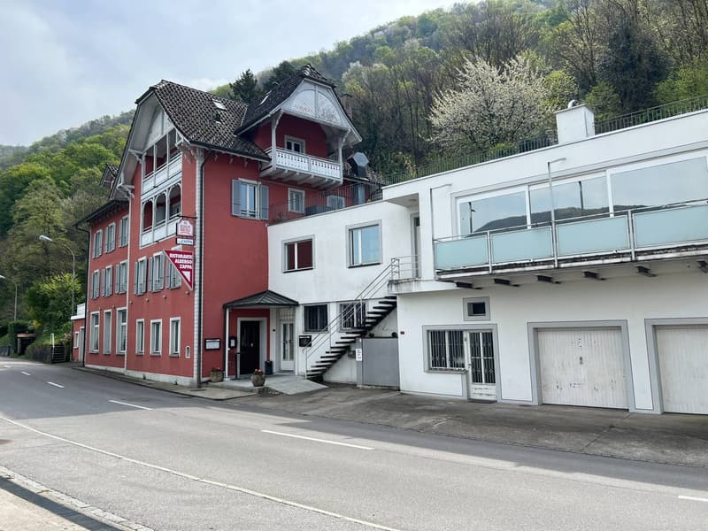 3 story building, red facade, white trim, balcony on the second floor, 2 garages