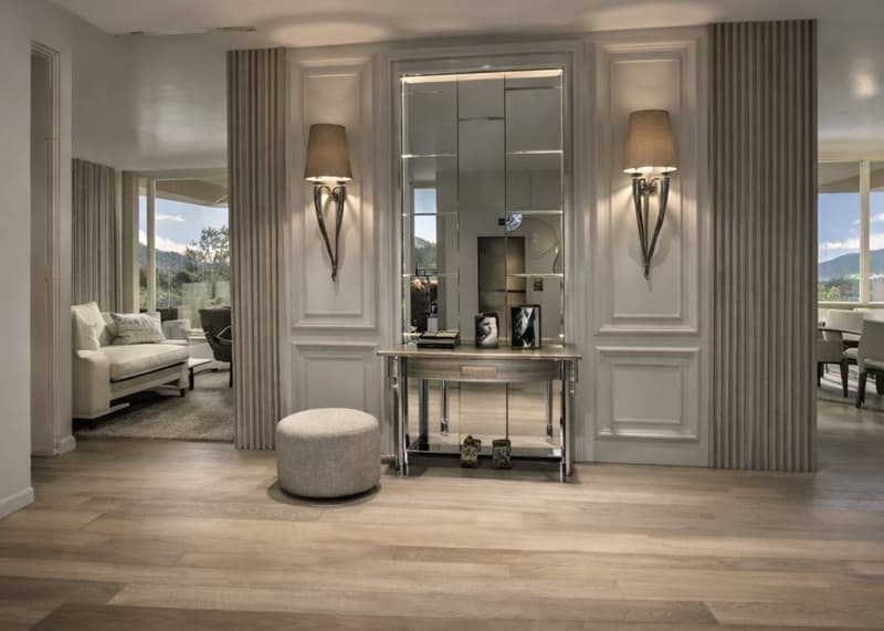 large mirror, large windows, hardwood floor, ottoman, table, lamps, couch, picture frames