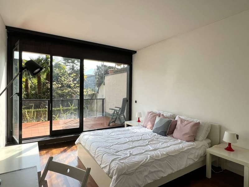white walls, wooden floor, large bed, white bedding, bedside tables, lamps, sliding glass doors, balcony