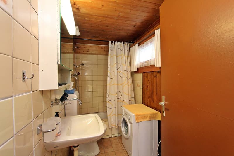 white tiled walls, white sink, white toilet, washing machine, wooden ceiling, window with white curtains