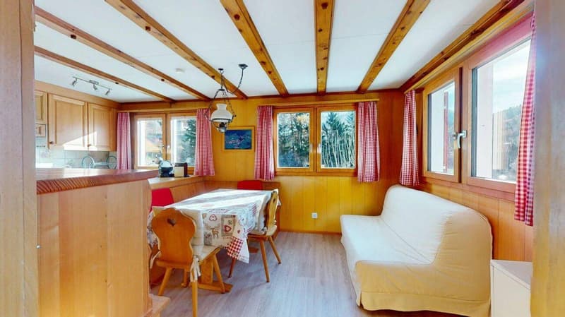 dining room with wooden table and chairs, sofa, wooden walls, windows with red curtains, wooden ceiling beams, view of trees outside