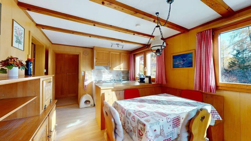 dining room with wooden walls, wooden floor, dining table, chairs, kitchen, flower vase, picture frames, clock, sink, faucet, coffee machine, window with red curtains