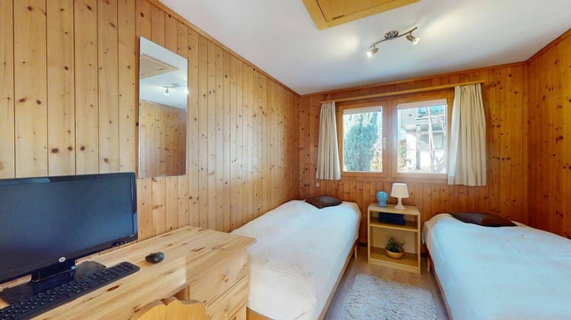 wooden walls, two single beds, desk with computer, mirror, nightstand with lamp, rug