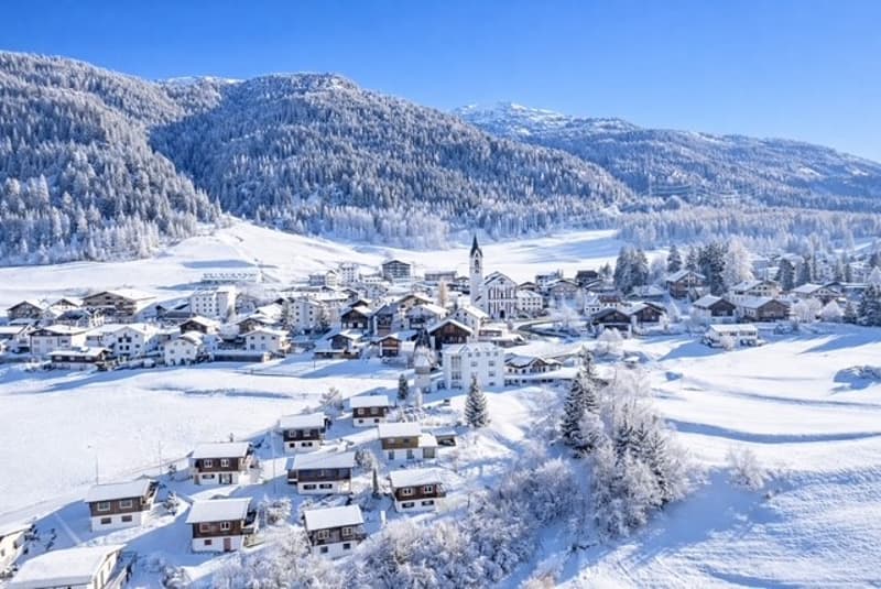 Mountain village with snow-covered houses, church, and pine trees