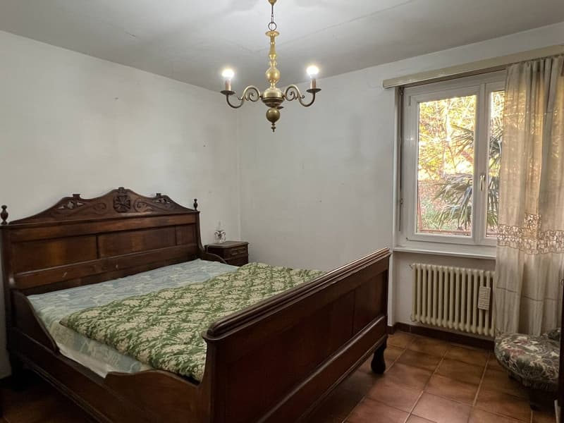 wooden bed, green bedspread, wooden nightstand, chandelier, radiator, window with curtains