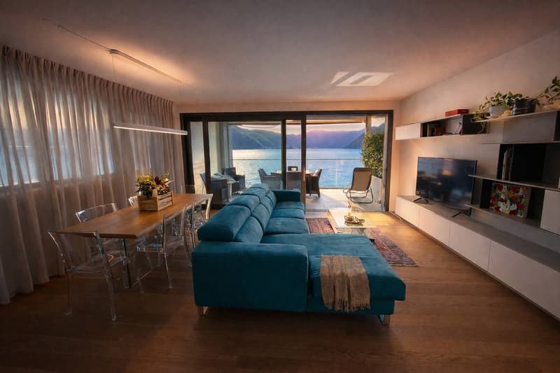 modern living room with blue sofa, wooden table, glass chairs, large windows, view of the sea