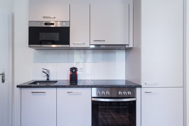 Modern kitchen with white cabinets, black granite countertop, built-in microwave oven, and stainless steel appliances including a dishwasher.