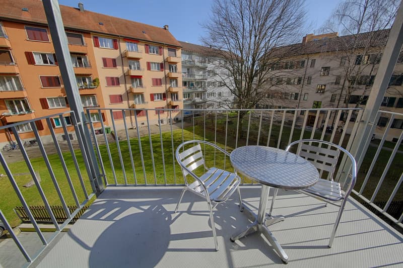 Balcony with outdoor furniture, overlooking a grassy area and multi-story apartment buildings