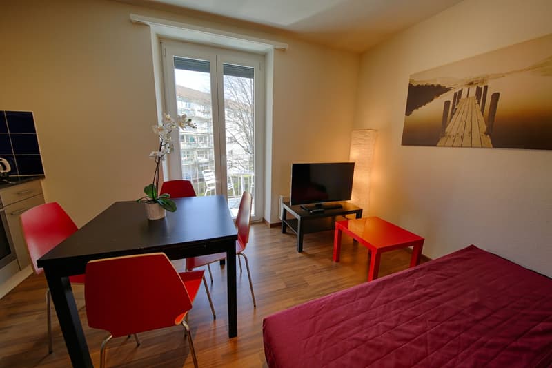 Spacious living room with large windows, hardwood floors, black dining table with red chairs, TV stand, and a red couch