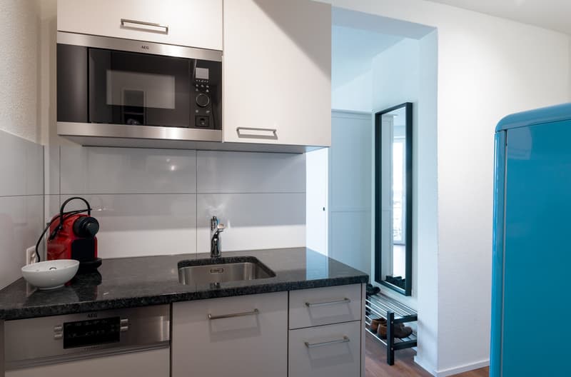 Modern kitchen with stainless steel appliances, including a built-in microwave oven and dishwasher. The kitchen has a granite countertop and a sink. There is a blue refrigerator visible in the background.