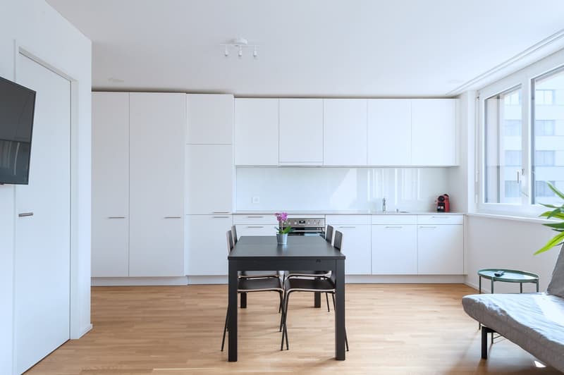 Spacious open-concept kitchen with white cabinets, black dining table and chairs, hardwood floors, and a dishwasher visible.