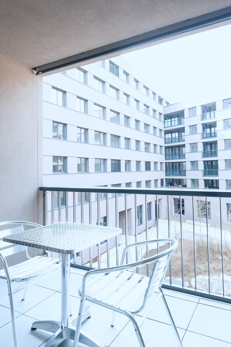 Balcony with a small table and chairs, overlooking a modern apartment building with many windows